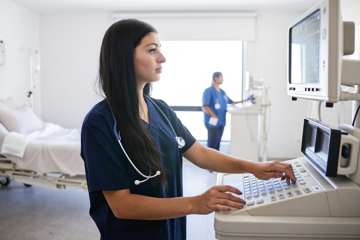 A hospital clinician entering readings at a vital-signs monitor